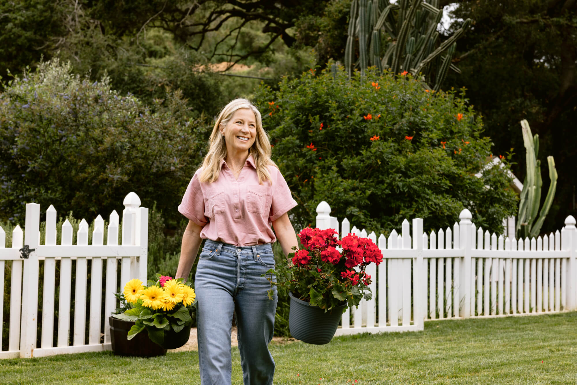 Woman walking outdoors with potted plants in a garden setting